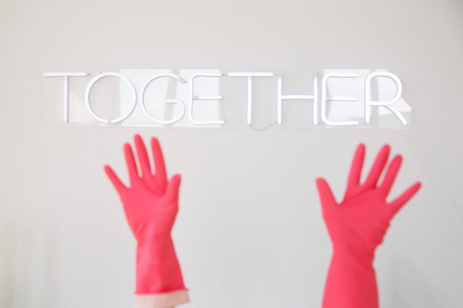 Red rubber-gloved hands reaching towards a white neon 'TOGETHER' sign, symbolizing unity and teamwork.