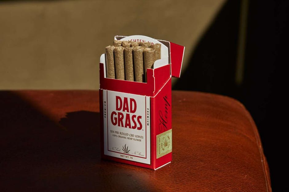 Red box of Dad Grass CBD joints displayed on a brown leather background.