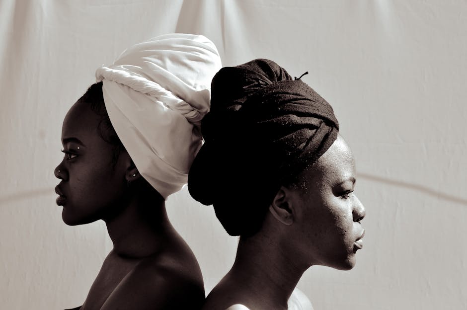 Monochrome side profile of two women with contrasting turbans in a conceptual pose.