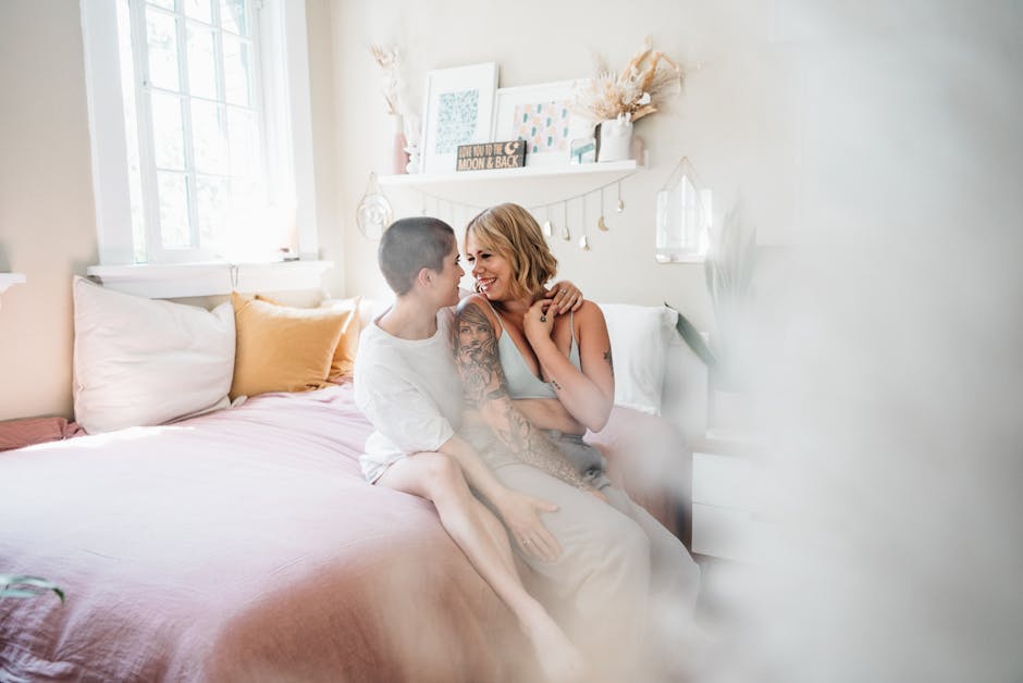 A loving LGBTQ couple shares a tender moment in a bright, cozy bedroom.