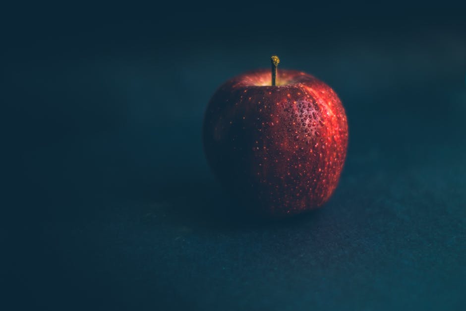A vibrant red apple with glistening water droplets on a dark backdrop, emphasizing freshness and natural appeal.