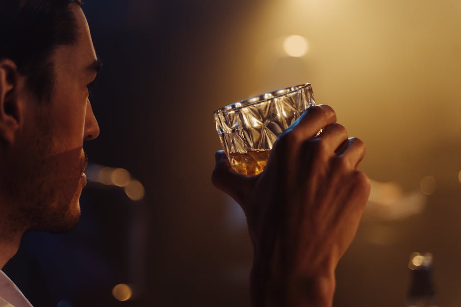A man holding a whiskey glass in a dimly lit bar setting, showcasing moody ambiance.