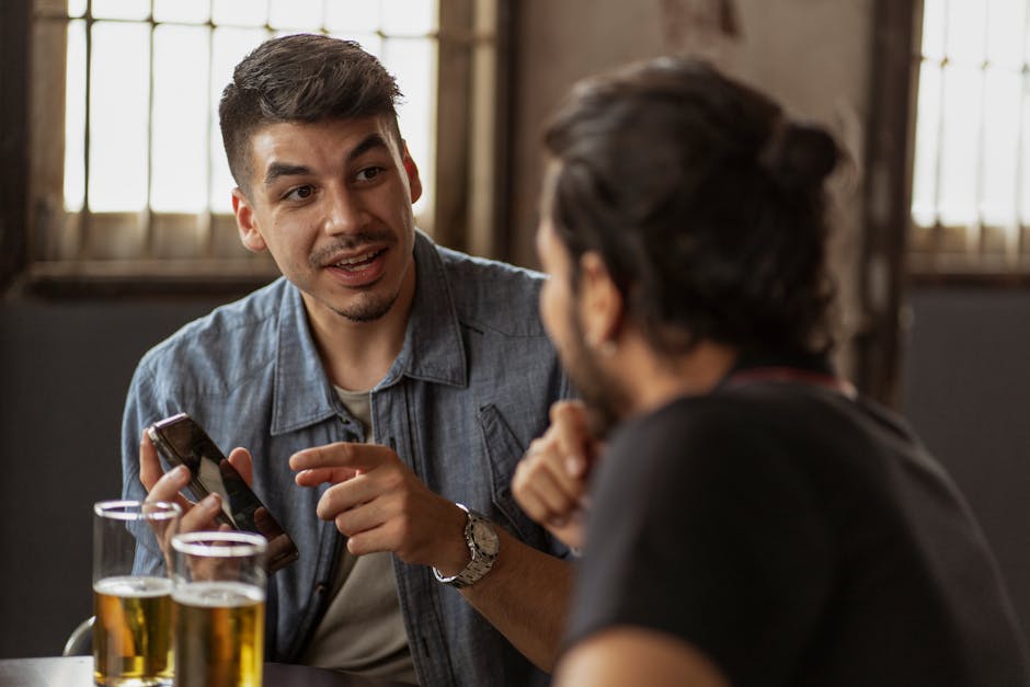 Two men engaged in conversation over drinks at a casual indoor setting, holding mobile phones.