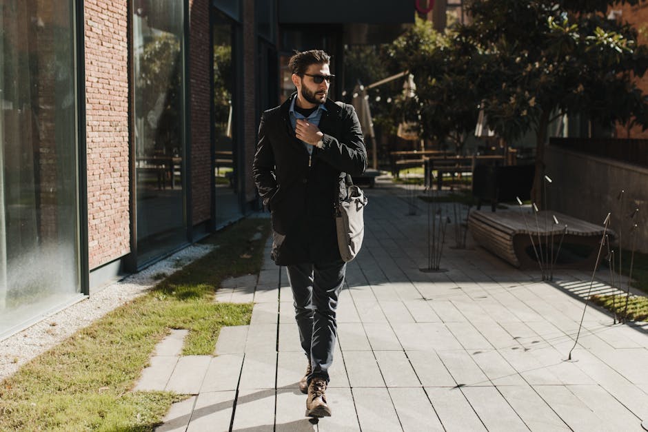 Stylish man with sunglasses and beard walking outside in urban environment.