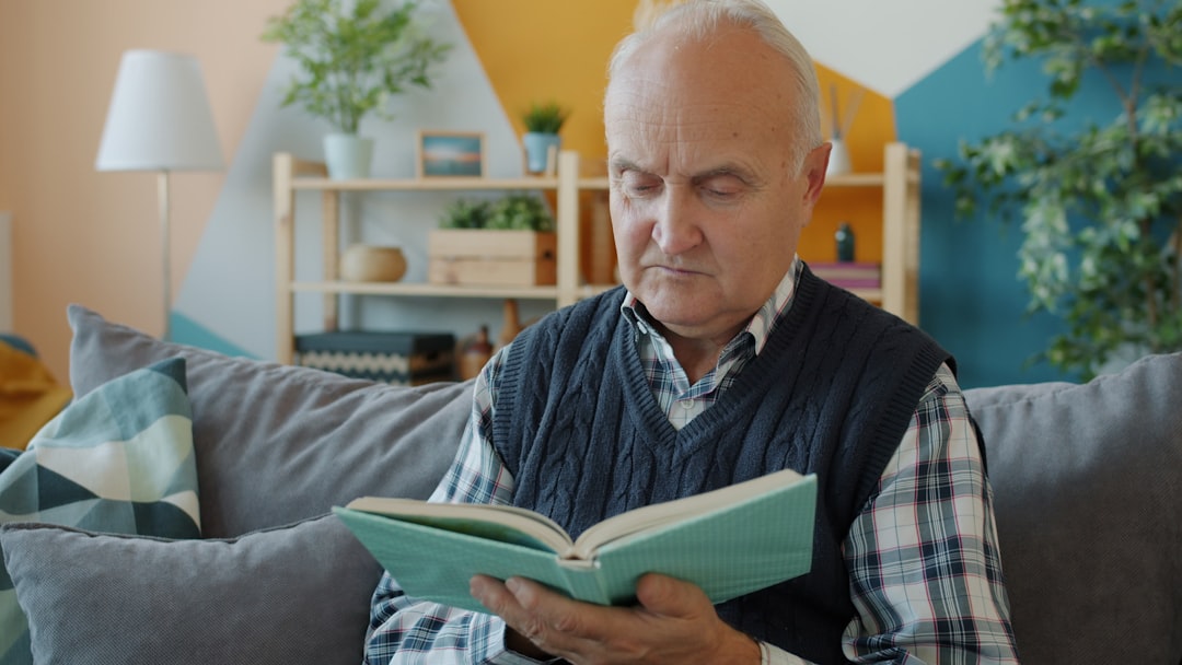 Elderly man reading a book on a couch.