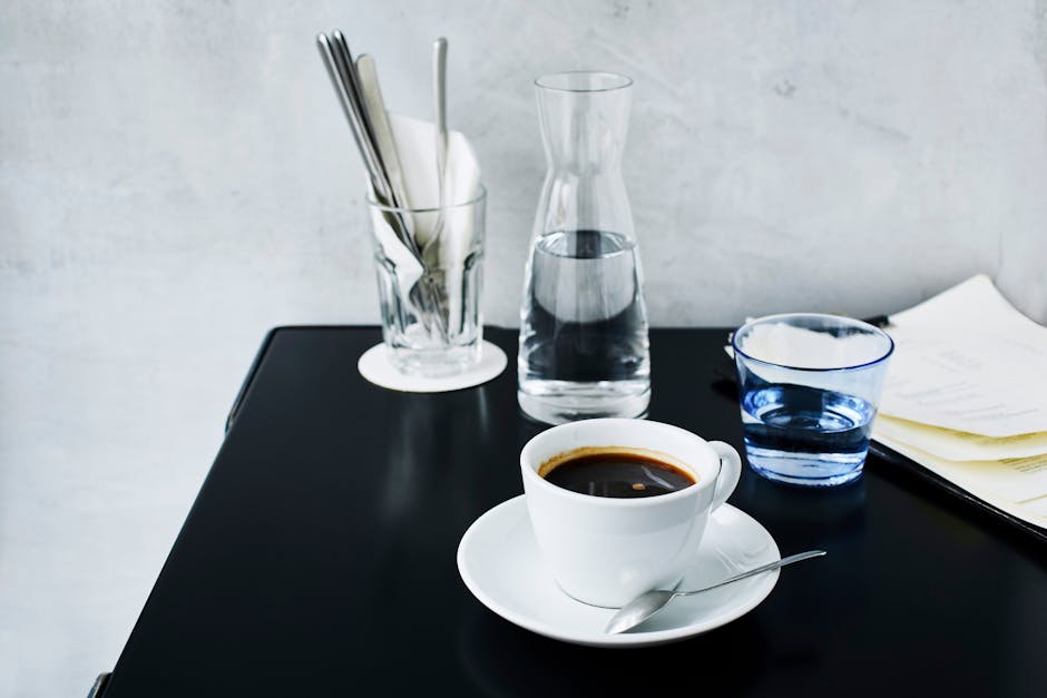 A minimalist cup of black coffee with water and utensils on a café table.