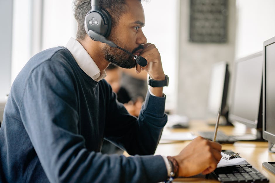 Side view of a bearded man in a headset concentrating at his desk in an office environment.