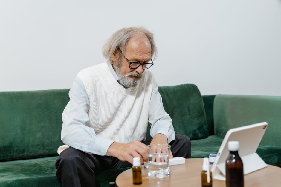 Elderly man sitting at home using a tablet for a telehealth consultation, surrounded by medicine.
