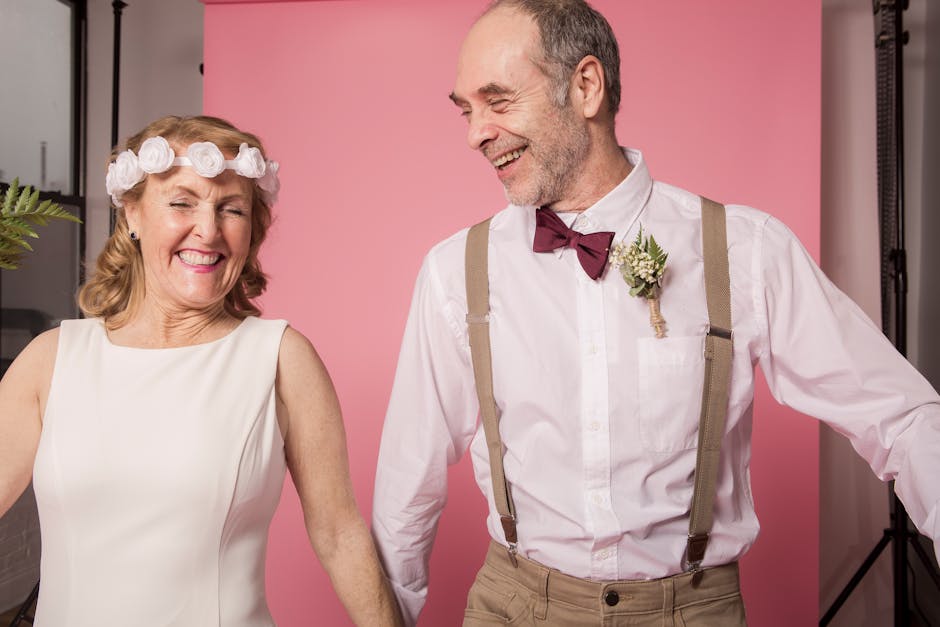 A happy senior couple embracing joyfully during a studio photo session with a pink background.