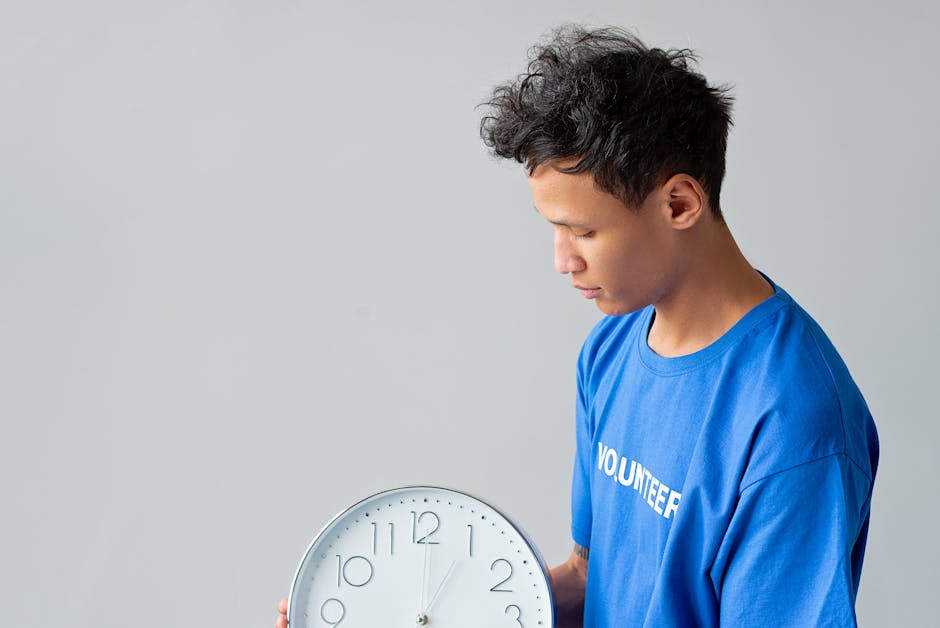 A young man in a blue shirt with 'Volunteer' on it holds a wall clock. Time concept.
