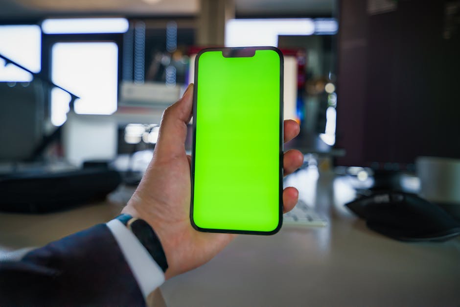 Close-up of a smartphone with a green screen held by a suited professional in an office setting.