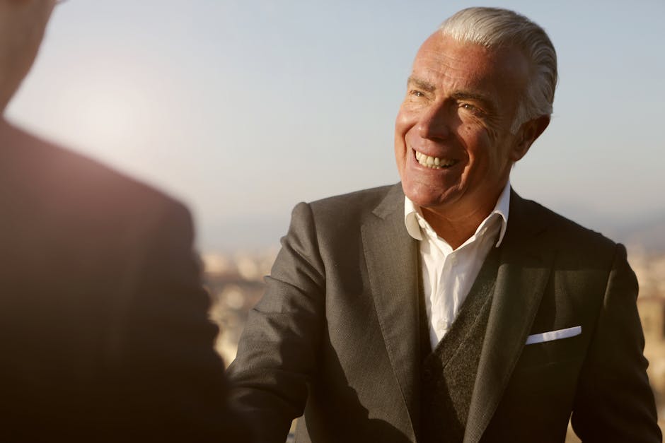 Elderly businessman smiling during a handshake outdoors. Warm, professional and engaging atmosphere.