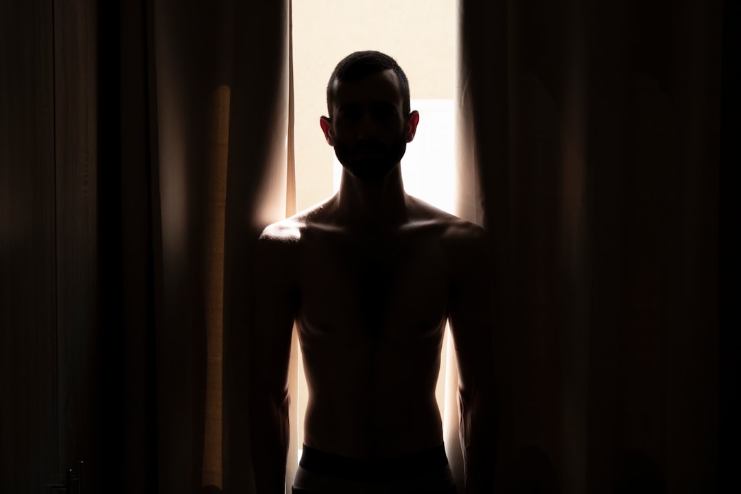 topless man in black shorts standing near window
