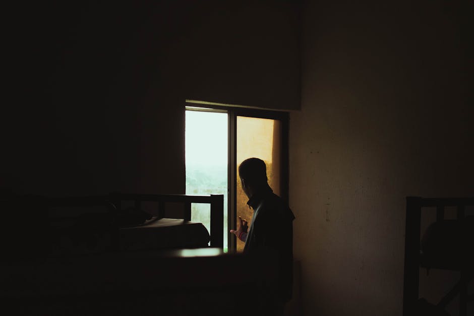 Silhouette of a man gazing out a window in a dimly lit room with bunk beds.