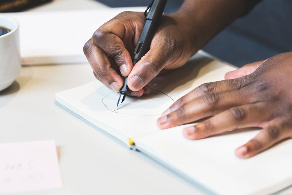 Close-up of a man writing with a fountain pen in a notebook, indoors.