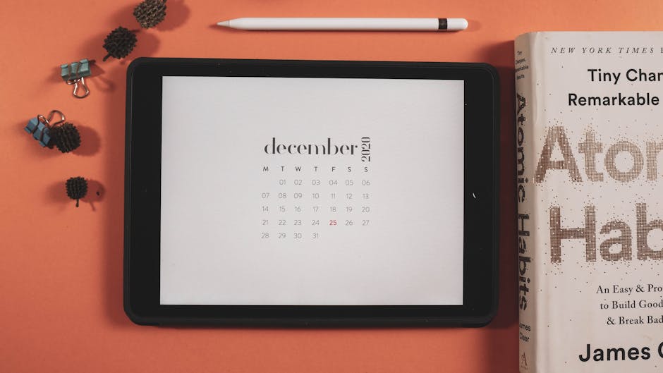 Minimalist flat lay featuring a tablet displaying a December 2020 calendar and a book.