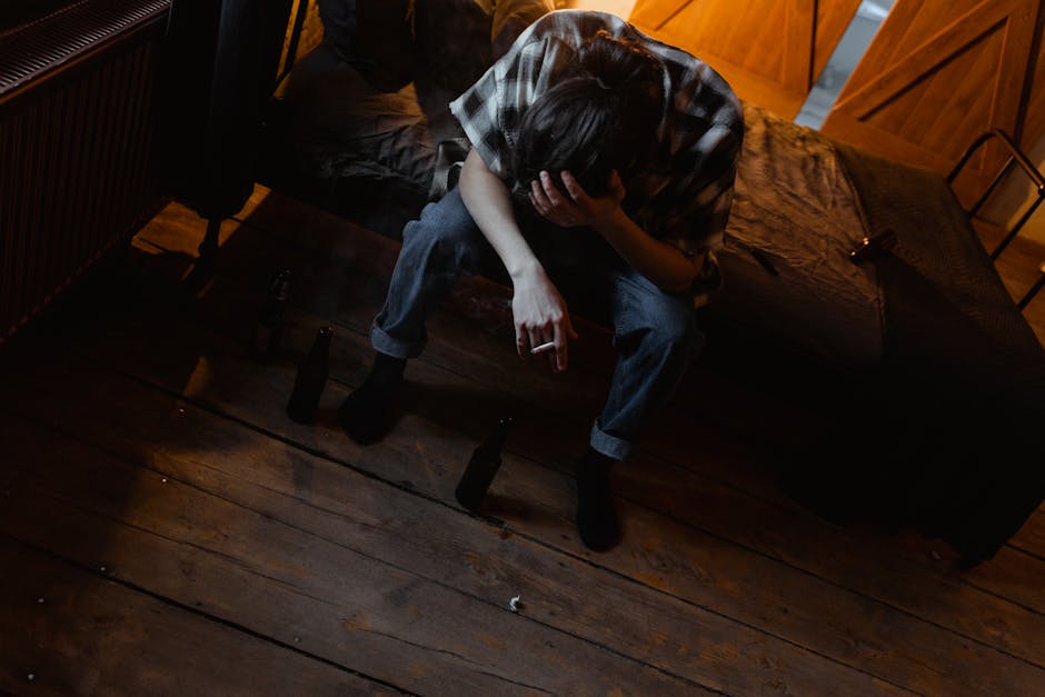 A young man sitting on a bed appears distressed, holding a cigarette in a dimly lit room.
