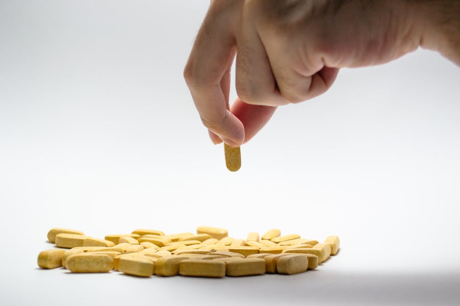 Close-up of a hand picking a yellow pill from a pile of tablets on a white surface.
