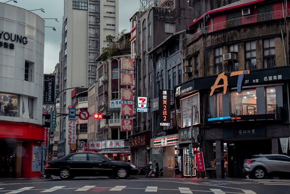 A vibrant urban street scene in Taipei featuring busy traffic and neon-lit storefronts at dusk.