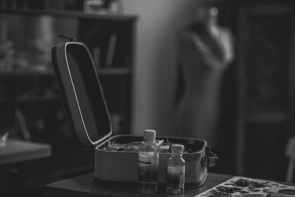 A black and white image of vials and an open box on a table, creating a moody still life scene.