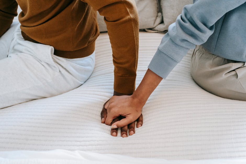A couple sits closely on a bed holding hands, symbolizing connection.