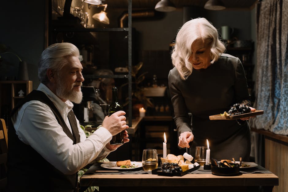Elderly couple enjoying a romantic candlelit dinner with wine and cheese in a cozy setting.