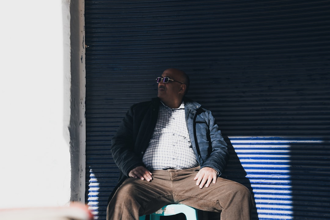 man sitting on plastic chair while leaning on black wall