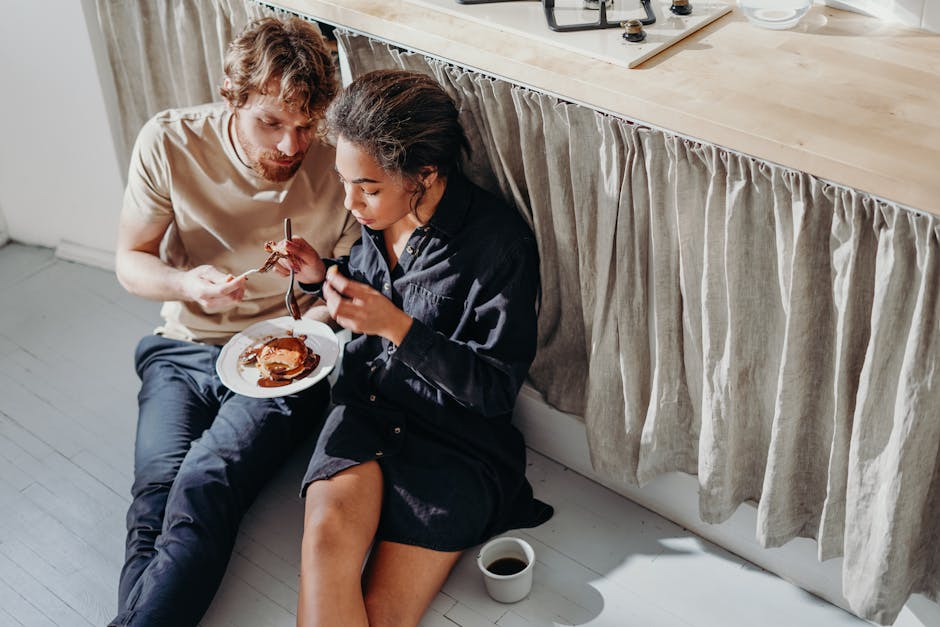 A couple enjoys a cozy morning breakfast with pancakes and coffee, sitting together on the kitchen floor.